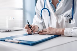 Doctor,Sitting,At,Desk,And,Writing,A,Prescription,For,Her