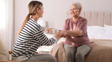 Young,Caregiver,Talking,To,Senior,Woman,In,Bedroom.,Home,Care